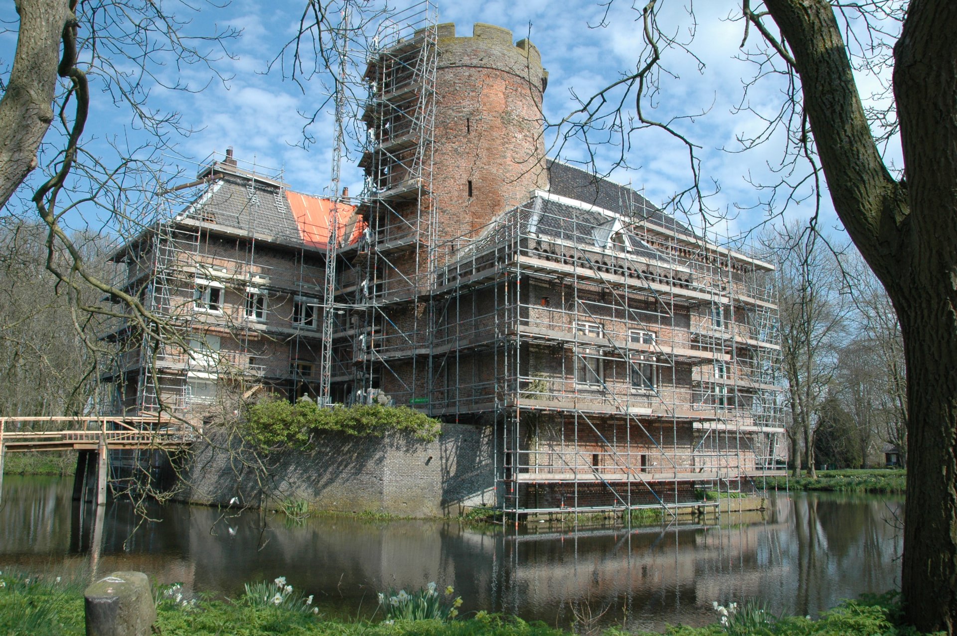 Het kasteel met de ronde toren in het najaar, gezien over een weide met schapen; hoge bomen met oranje blad staan voor de gevel