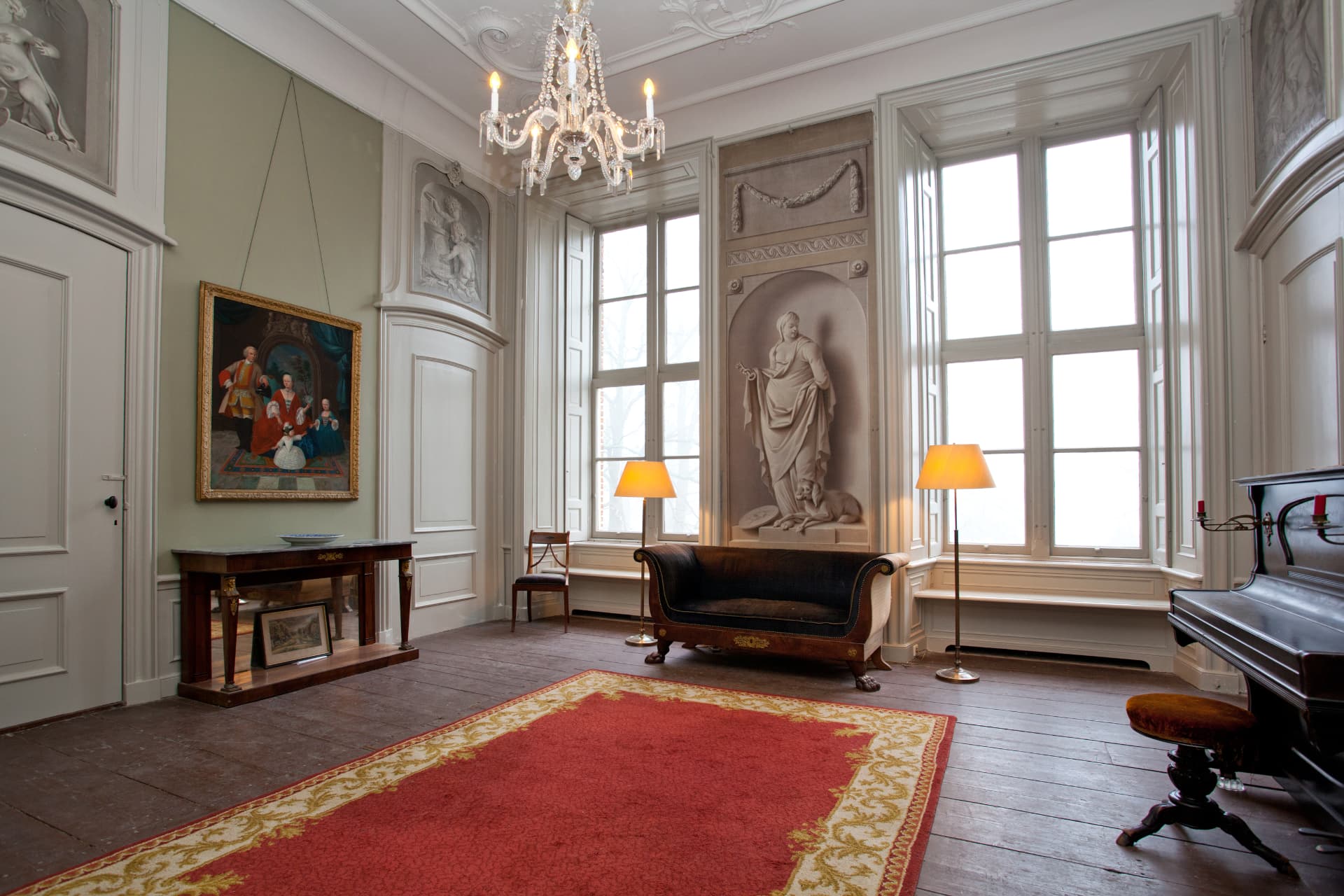 De salon met grisailleschildering, kroonluchter, sofa en vleugel