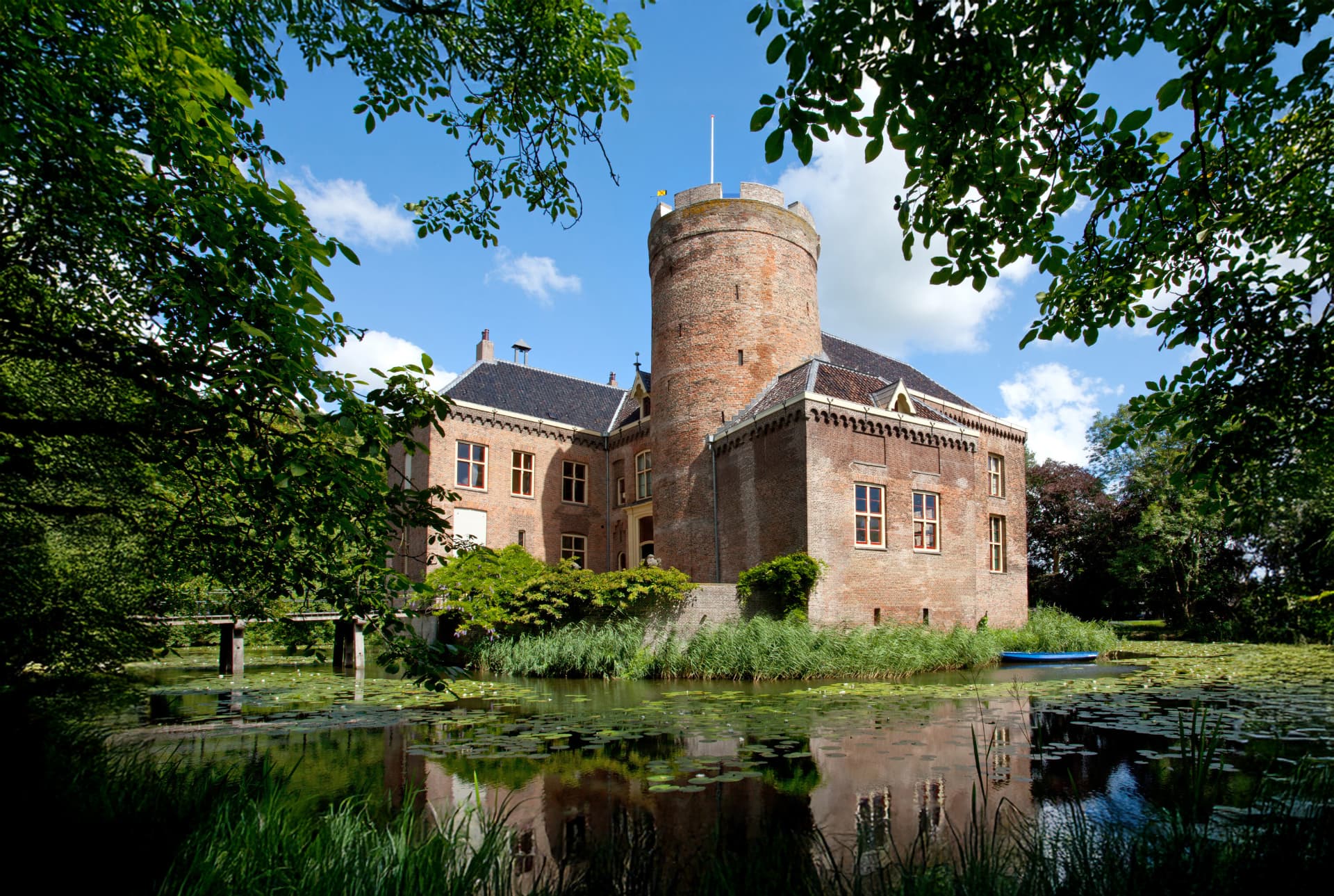 Kasteel Loenersloot met ronde toren, verscholen achter groen en weerspiegeld in de gracht