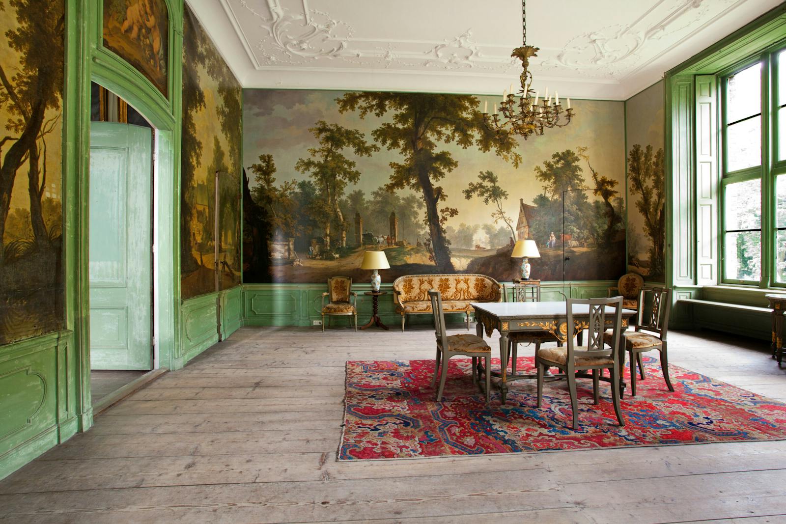 De tuinkamer met geschilderde landschapsbehangsels, tafel en kroonluchter